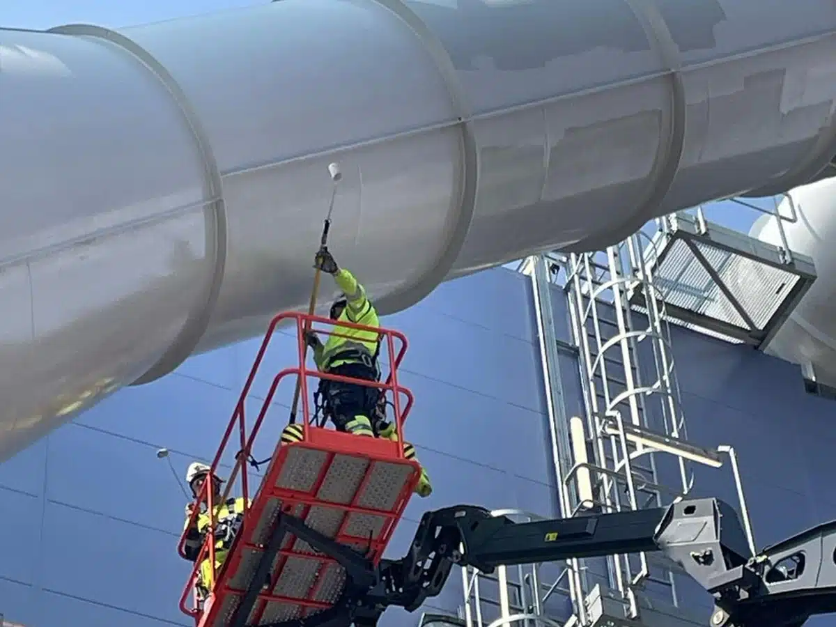 Rope access technicians on mewp applying top coat paint to industrial energy for waste facility