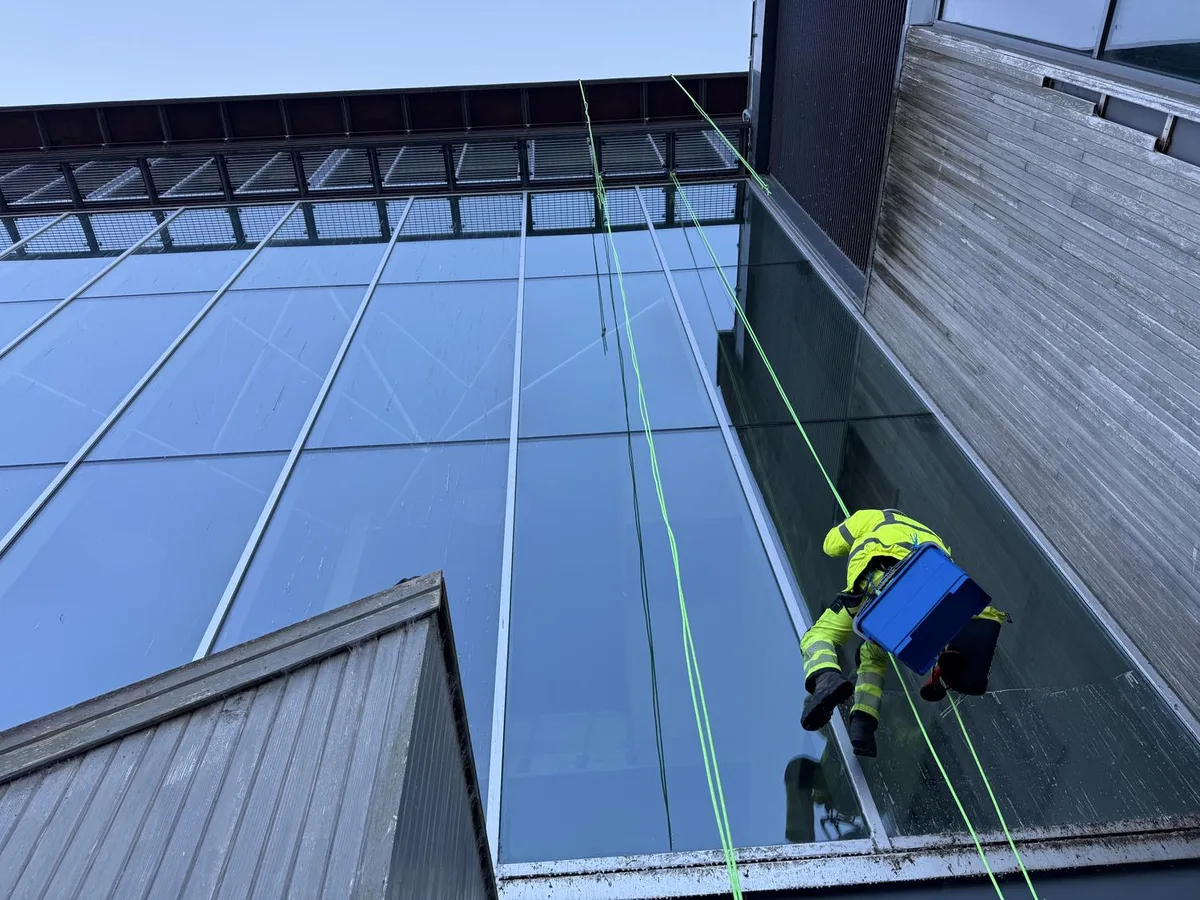 Technician abseiling down the glass facade during high level cleaning