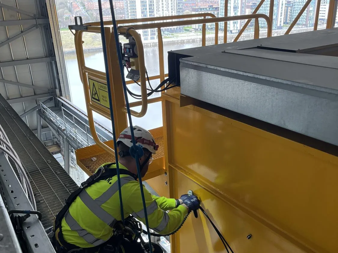 Technician carrying out earthing works on an overhead crane by rope access