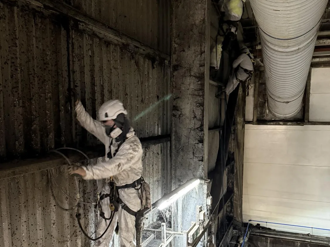 Technician in respiratory protection cleaning ductwork by rope access